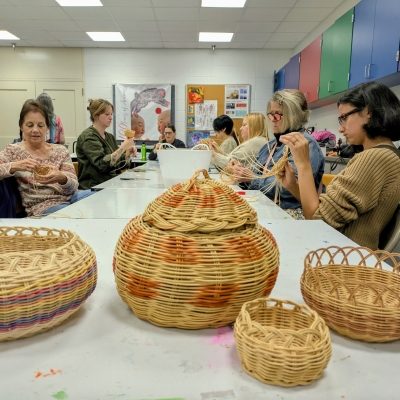 People sitting at a table, weaving baskets